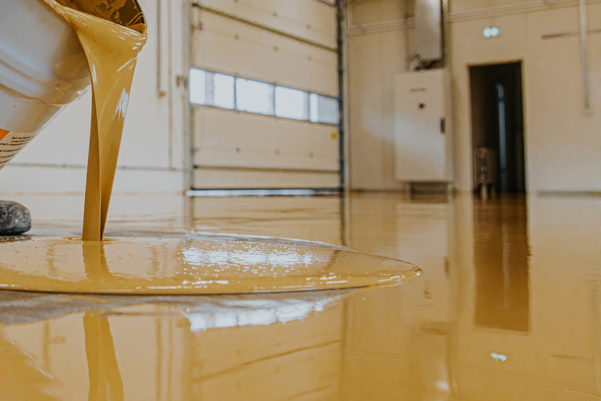 Worker, coating floor with self-leveling epoxy resin in industrial workshop.